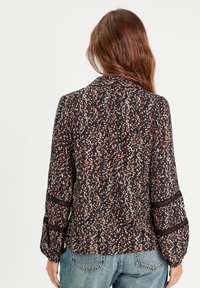 Blouse fluide à manches longues en tissu noir, avec un motif floral coloré, un col arrondi et des détails en dentelle sur les manches.