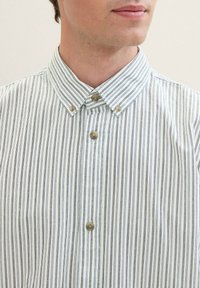 Camisa de botones con estrechas rayas verticales en blanco y azul marino. Presenta un cuello clásico, dos botones en el cuello y una textura suave.