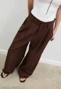 Bruna byxben i vid modell av ett strukturerat tyg, med framvik och fickor. Matchade med en figurnära vit topp och enkla sandaler.