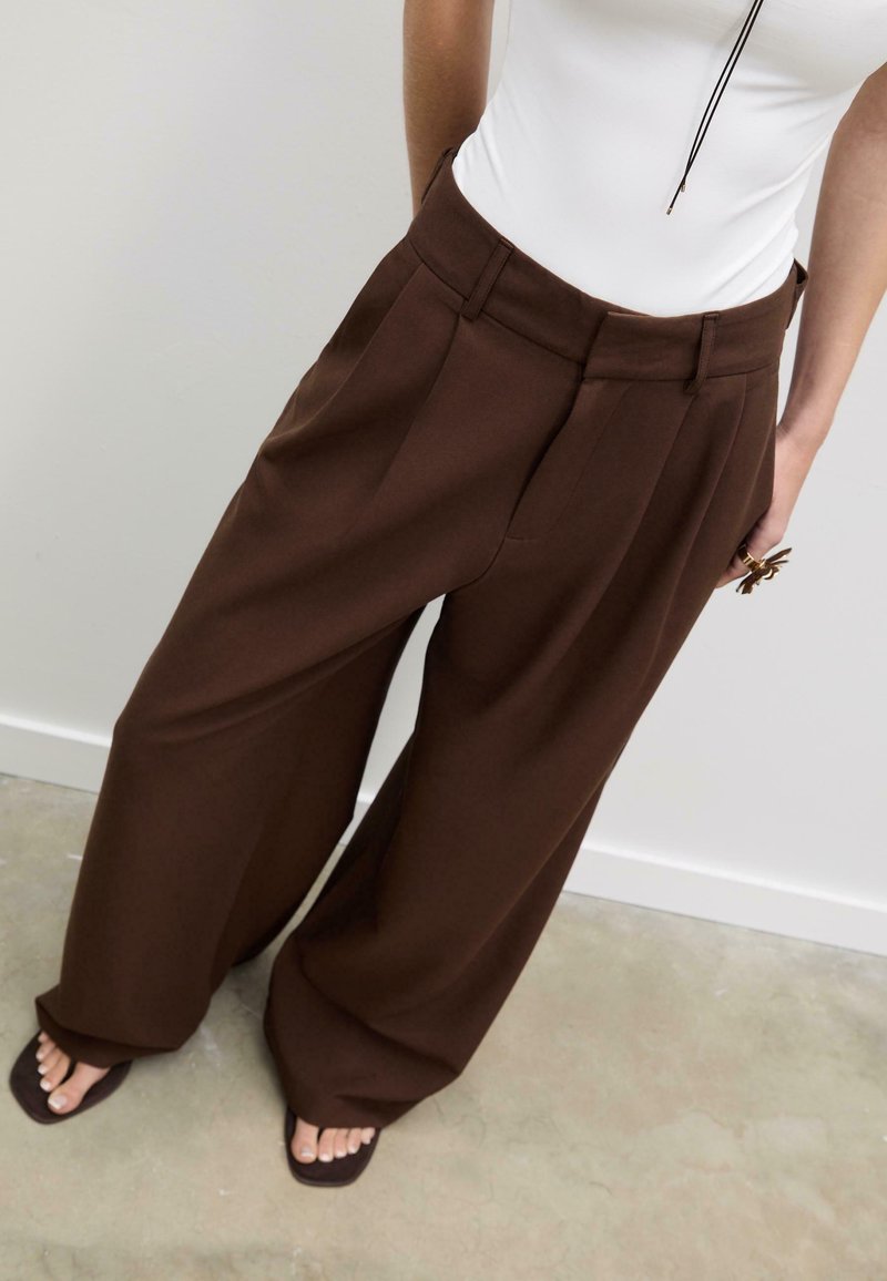 Bruna byxben i vid modell av ett strukturerat tyg, med framvik och fickor. Matchade med en figurnära vit topp och enkla sandaler.