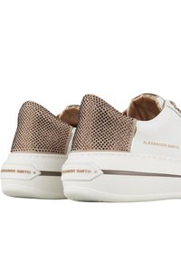 Sneaker bianche con pannelli di tacco beige borchiati, suole bianche spesse e branding "Alexander Smith" sul lato e sul tallone.