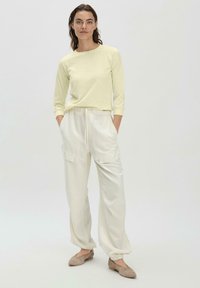 Hellgelbes Oberteil mit langen Ärmeln und rundem Ausschnitt, kombiniert mit lockeren weißen Cargo-Hosen mit seitlichen Taschen und elastischen Bündchen. Beige Ballerinas.