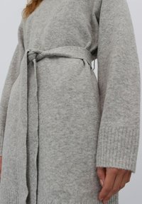 Grauer Strickpullover mit abnehmbarem Gürtel in der Taille, weichem Material, gerippten Bündchen und lässiger Passform.
