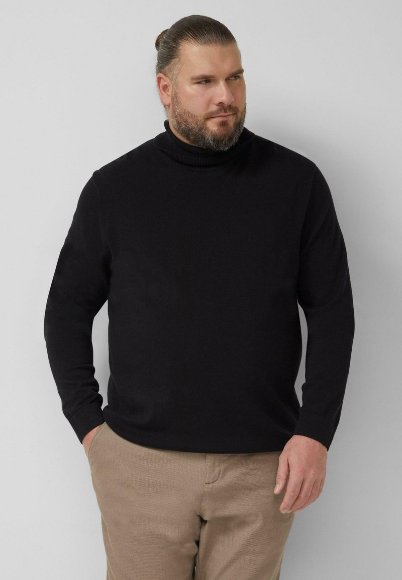 Schwarzer Rollkragenpullover aus einem weichen Stoff, mit langen Ärmeln und gerippten Details am Kragen und an den Bündchen; kombiniert mit beigen Hosen.
