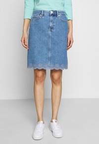 Džínová áčková sukně v světle modré barvě, střední délky s vykrojeným lemem, který má výšivku s otvorovými vzory. Pět kapes a přední zapínání na knoflíky.