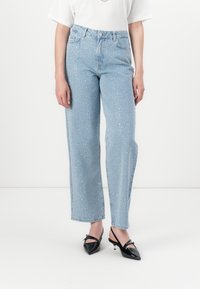 Ανοιχτό μπλε παντελόνι με φαρδιά γραμμή και ψηλή μέση, με σπασμένο μοτίβο και κλασικό σχέδιο πέντε τσέπες. Φοριέται με μαύρες γόβες με τακούνι.