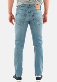 Jeans de mezclilla de color azul claro con un corte recto, cinco bolsillos y costuras en contraste. Presenta un parche de cuero en la parte trasera con el logotipo de la marca.