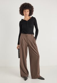 Sort ribbet zip-up top med en bred krave, parret med brune brede bukser. Sættet er suppleret med en sort nitter-clutch og spidse sko.