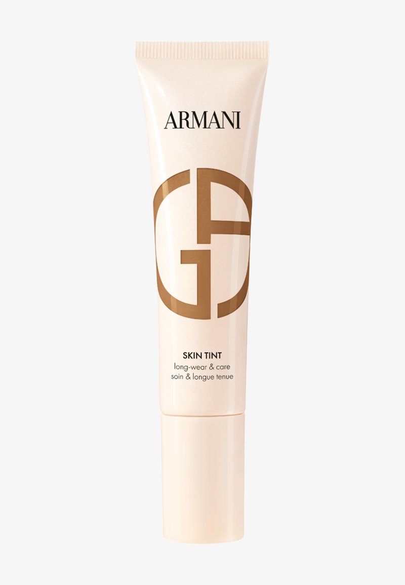 Beige-farget hudpleietube med hvit kork. Har svart "ARMANI"-tekst og en stor brun logo. Teksten sier "SKIN TINT langvarig og pleie."