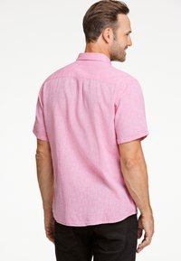 Korte mouwen shirt van lichtroze stof met een gestructureerde look, voorzien van een knoopsluiting bij de kraag en een gebogen zoom. Zwarte broek zichtbaar.