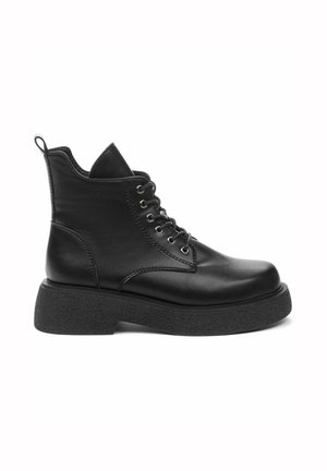 Bottine en cuir noir avec semelle épaisse texturée, devant à lacets et languette au talon, montrée de profil sur fond blanc.
