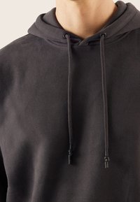 Ciemnoszara bluza z kapturem wykonana z miękkiej tkaniny, z kieszenią kangurką i kapturem ze ściągaczem z czarnymi końcówkami. Gładka faktura z minimalną ilością szwów.