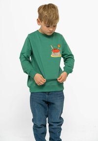 Grön sweatshirt med en mat-tematisk grafik som föreställer spaghetti och köttbullar, i kombination med blå denimjeans. Mjuk, avslappnad design.
