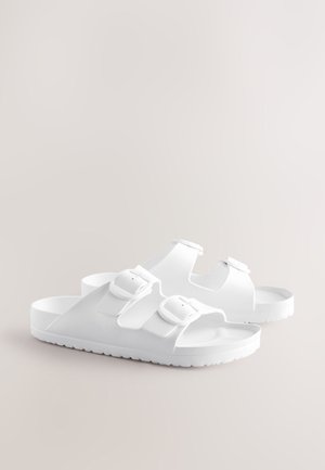 Valged sandaalid kummitaolise materjaliga, kaks reguleeritavat rihma ja pandlaga sulgemine, musterdatud tallaga, et parandada haarduvust.