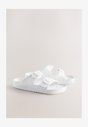 Valged sandaalid kummitaolise materjaliga, kaks reguleeritavat rihma ja pandlaga sulgemine, musterdatud tallaga, et parandada haarduvust.