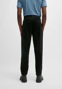 Czarne spodnie sztruksowe o fakturowanej powierzchni, z tylnymi kieszeniami i elastycznymi mankietami. Noszone z niebieską koszulą z krótkim rękawem i czarnymi butami.