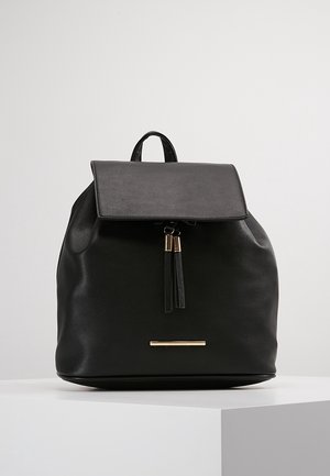 Zwarte leren rugzak met klepsluiting, twee zwarte kwastjes met gouden accenten en een kleine horizontale gouden stang aan de voorkant.