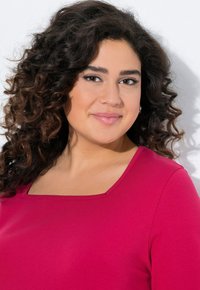 Haut fuchsia avec un col carré, en tissu lisse. Le modèle a des cheveux bouclés, et l'éclairage met en valeur la texture et la couleur.
