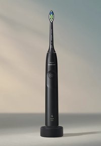 Spazzolino elettrico con manico nero, base di ricarica circolare, pulsante di accensione ben visibile e testa del pennello stretta con un design verde e blu.