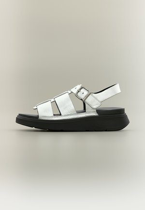 Sandalo in pelle bianca con tre cinturini, fibbia regolabile e suola nera spessa su uno sfondo neutro chiaro.