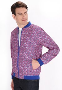 Giacca bomber da uomo con un vivace motivo geometrico rosa e blu, caratterizzata da un colletto e polsini blu a coste, e tasche laterali.