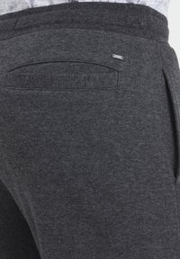 Pantalons de survêtement gris foncé en tissu doux, avec une poche arrière et des détails de couture subtils. Ceinture élastique pour plus de confort.