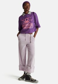 Sudadera corta morada con estampado gráfico y cuello gris; pantalones anchos a rayas en lavanda; zapatillas negras con detalles grises.