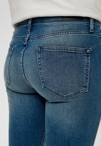 Blakniejące niebieskie dżinsy o dopasowanym kroju. Posiadają tylną kieszeń o spiczastym kształcie i subtelnym detalu w szyciu.