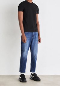 Camiseta de algodón negra, jeans de denim azul con corte recto y zapatillas negras con acentos blancos, presentados sobre un fondo neutro.