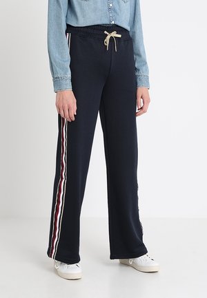 Marina blå sweatpants med dragkedja i midjan, med vertikala ränder i röd, krämfärg och kastanje längs sidorna. Mjuk tyg, avslappnad passform.
