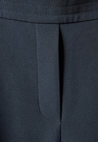 Donkerblauwe op maat gemaakte broeken hebben een gladde stof met een subtiele textuur, een voorplooim en nette stiksels langs de tailleband.