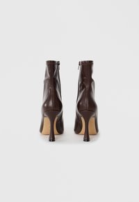 Bottines en cuir marron avec un design épuré, dotées d'une fermeture éclair à l'arrière et de talons aiguilles hauts. Texture lisse et détails de couture minimes.