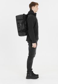 Musta reppu, jossa on suorakulmainen muoto, valmistettu kestävästä materiaalista, sisältää logokyvyn ja useita hihnoja turvallista käyttöä varten.