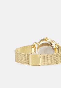 Gold mesh band watch with a round case, featuring a metallic finish and a clasp with the "TIMEX" logo engraved. Back is transparent.