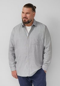 Camicia a righe grigie e bianche con taschino sul petto e maniche con risvolto, realizzata in un tessuto leggero. Indossata sopra una maglietta bianca.