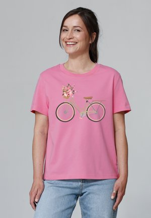 T-shirt en coton rose avec un graphisme d'une bicyclette avec un panier de fleurs. Manches courtes et coupe décontractée, associé à un jean bleu clair.