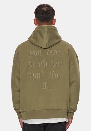 Olivengroene hoodie van zacht stof, met een ruime capuchon en grote geborduurde tekst op de achterkant. Afgeronde zoom en een ontspannen pasvorm.