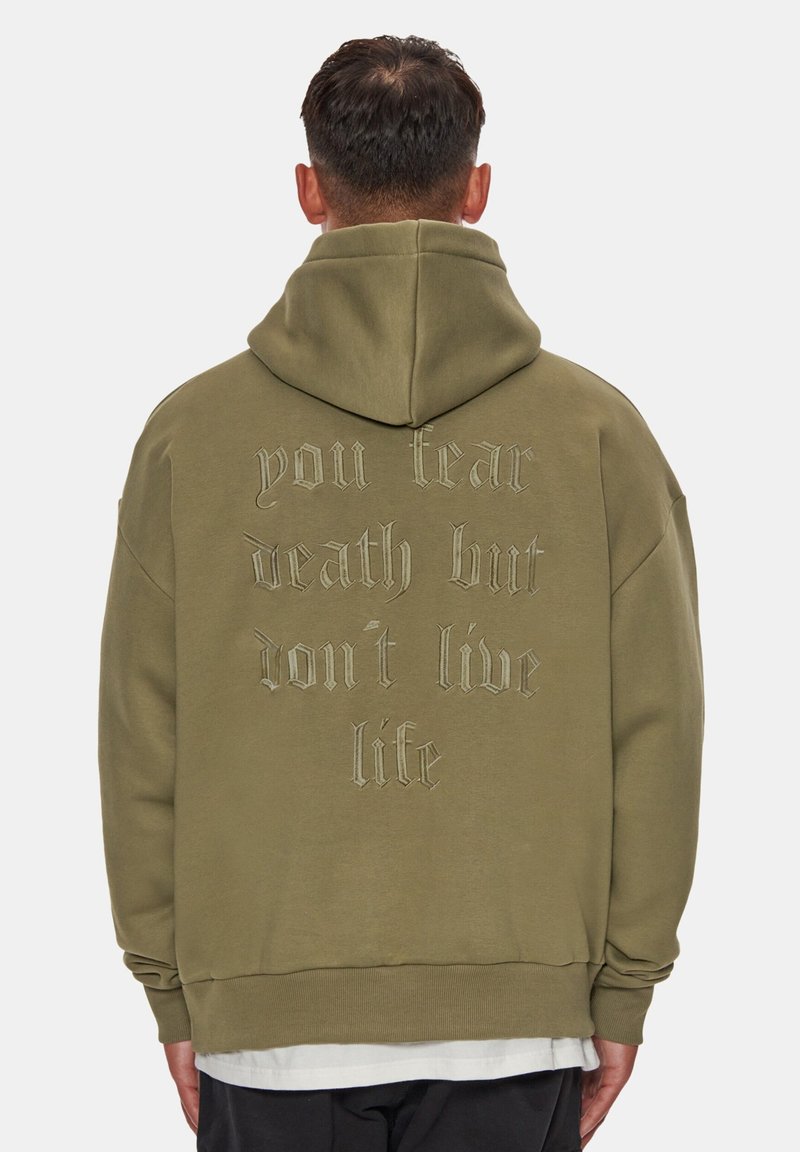 Felpa con cappuccio verde oliva realizzata in tessuto morbido, con cappuccio ampio e grande scritta ricamata sulla schiena. Orlo arrotondato e vestibilità comoda.