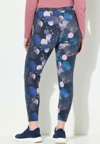 Leggings multicolori presentano uno sfondo scuro con motivi astratti di cerchi blu, rosa e grigi, realizzati in un tessuto elastico con una superficie liscia.