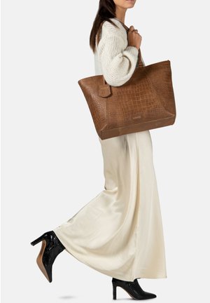 Bruine leren tote bag met een krokodillenstructuur, voorzien van een vlakke bodem en een verwijderbaar label. Gestyled met een crèmekleurige sweater en een vloeiende beige rok.