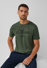 Zelené bavlnené tričko s čiernym logom s nápisom "s.Oliver ELEVATED ESSENTIALS SINCE 1969." S okrúhlym výstrihom a krátkymi rukávmi.