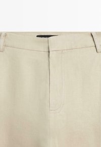 Pantalon beige taille haute avec passants de ceinture et fermeture éclair avant cachée, confectionné dans un tissu lisse.