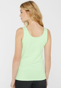 Hellgrünes Tanktop mit rundem Hals, ärmellosem Design und glatter Textur. Es hat eine figurbetonte Form und einen Saum, der auf Taille fällt.