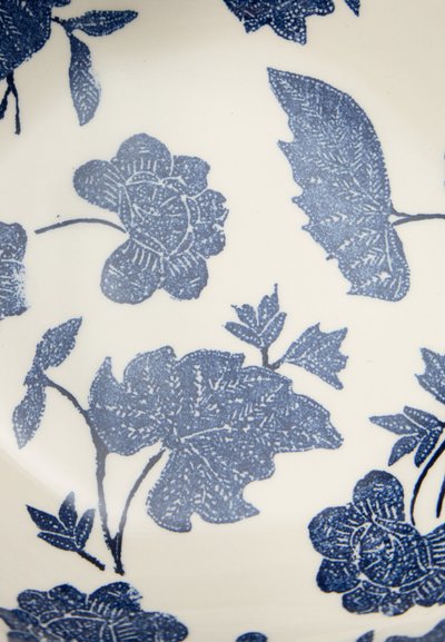 Γαλάζια λουλουδένια και φυλλώδη μοτίβα με λεπτομερείς διακοσμήσεις σε μια λευκή κεραμική επιφάνεια, που θυμίζουν σχέδιο vintage πορσελάνης.