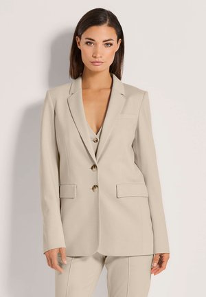 Beige blazer van een gladde stof, voorzien van een gecentreerde revers, drie knopen en twee voorzakken met een getailleerde pasvorm.