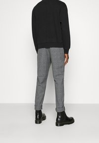 Sudadera negra, pantalones grises con estampado y botas negras con tacón. Los pantalones tienen un diseño a cuadros; la sudadera tiene un dobladillo acanalado.