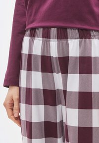 Μακρυμάνικη μπλούζα σε μωβ χρώμα συνδυασμένη με καρό παντελόνι σε μπορντό και λευκό χρώμα, με ελαστική μέση και απαλό βαμβακερό ύφασμα.