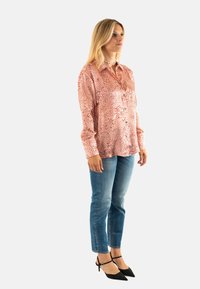 Camisa de estampado paisley rojo, hecha de una tela ligera, combinada con jeans de denim azul y tacones negros de punta. Diseño ajustado.