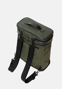 Sac à dos vert olive à design rectangulaire, en tissu et cuir, avec fermeture éclair, poignée supérieure et bretelles noires ajustables.