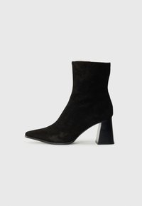 Bottines en daim noir avec un bout pointu, dotées d'un talon bloc noir texturé et d'une coupe ajustée autour de la cheville. Surface lisse.